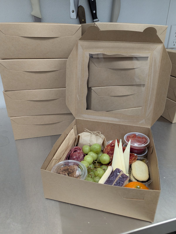 Individual charcuterie boxes sitting on a stainless steel counter
